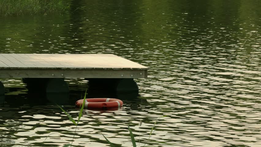 Red life preserver sits on a dock in the water. The water is calm and the dock is wooden
