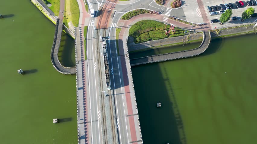 Aerial view of a modern tram curving through a roundabout, surrounded by lush green spaces and roads, Nieuwpoort, Belgium.