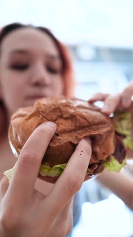 Teenage girl eating hamburger in fast food cafe. Fast food concept.