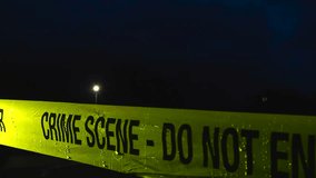 Police caution Crime Scene Do Not Enter yellow colored tape ribbon pulled in front of a dark nature area during night time while raindrops fall on the tape in slow motion, bokeh lights in the back. - Powered by Shutterstock - Get 15% off with code: PIKWIZARD15