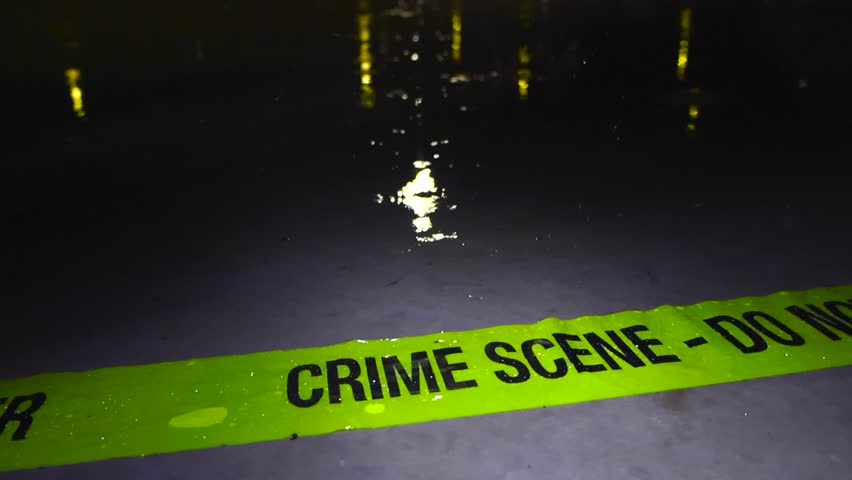 Close up slow motion footage of a police investigation forensics yellow colored Crime Scene tape ribbon abandoned on a concrete outdoors ground at night time while heavy rainfall is splashing on it.