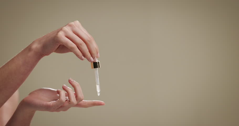 Skincare, dropper and serum on hands for beauty, dermatology and glow. Finger, pipette and woman apply cosmetic product or hyaluronic acid for anti aging on studio background with mockup space