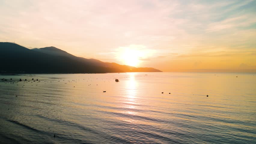 Golden sunrise illuminating calm sea near da nang, vietnam, with mountain silhouettes enhancing tranquil coastal landscape