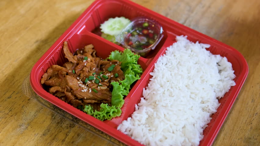 Rice pork vegetables Thai street food lunch boxes with jasmine rice, stir-fried vegetables, meat, and fried egg, neatly packed in clear plastic containers, displayed on a market stall