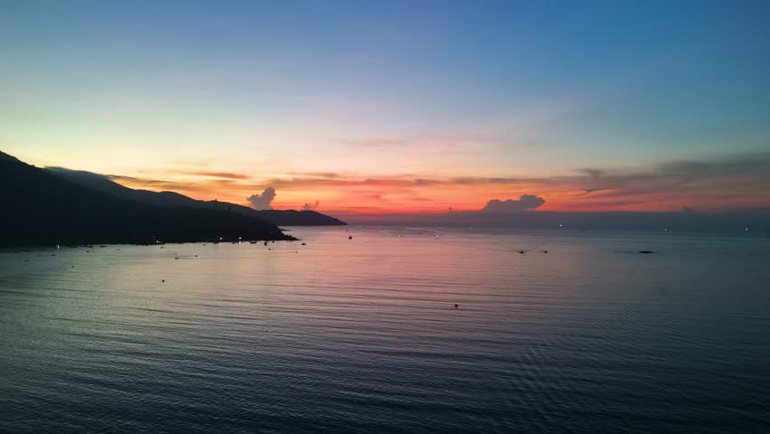 Wooden fishing boats sailing calm waters during golden sunset, son tra peninsula silhouetted against vibrant sky in da nang, vietnam marine landscape