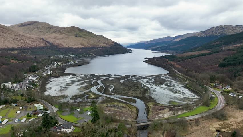 Aerial view of Loch Long, its calm waters reflecting the overcast sky, contrasting with the rugged terrain and the winding river channels, Arrochar, Scotland, Scotland.