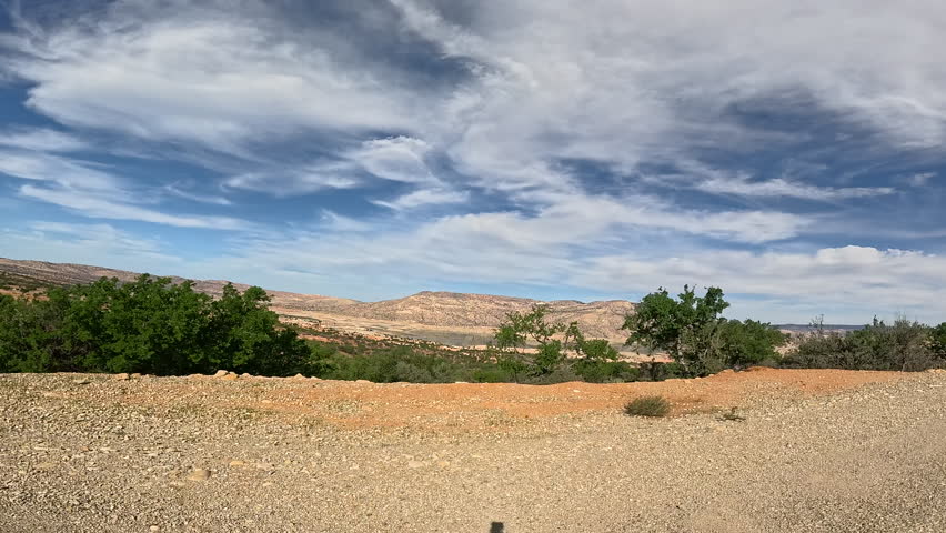 Travel through arid landscape with rolling hills and sparse green vegetation under blue skies with scattered clouds. Dry, rocky terrain in remote area of Morocco offers a sense of natural beauty.