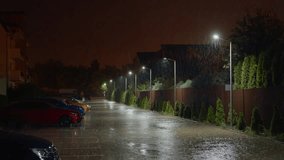 Intense rain falls on parked cars and residential homes during a nighttime storm. Strong winds and occasional lightning add to the dramatic weather conditions in the area. - Powered by Shutterstock - Get 15% off with code: PIKWIZARD15