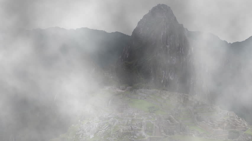 The ancient Incan city of Machu Picchu shrouded in and appearing from fog.