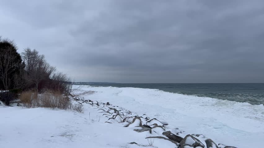 Frozen Lake Michigan shoreline with ice chunks and overcast skies. Cold winter scene capturing the moody atmosphere and icy lake water along the coast.