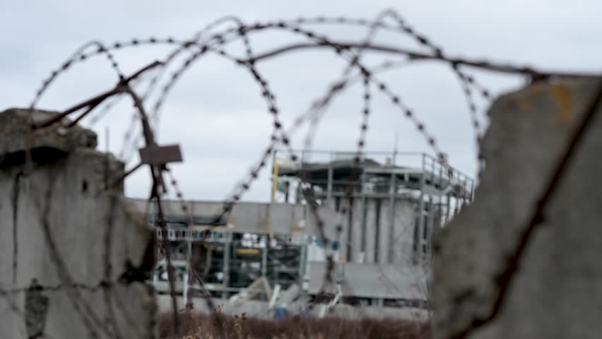 A destroyed factory on the outskirts of Kramatorsk is seen through a broken fence and tangled barbed wire. A stark view of the industrial damage caused by the war in Ukraine.
