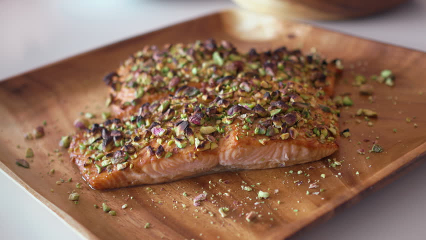 Grilled salmon fillets topped with crushed pistachios served on wooden plate. Delicious and healthy dish highlighting the combination of fish and nuts for nutritious meal