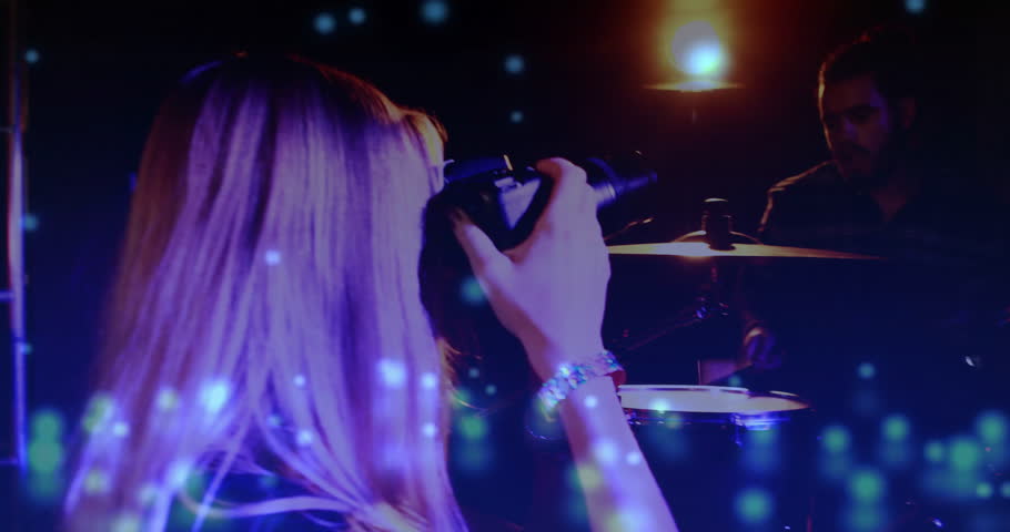 Woman raising camera activating blue overlay as filming drummer and vocalist for music promo. Concert, stage, performance, artist, instrumentation, lighting, multimedia