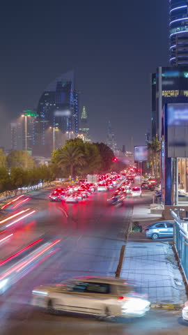 Aerial night timelapse of Riyadh, Saudi Arabia, featuring illuminated towers, skyscrapers, King Fahd Road and busy traffic. Palms and streetlights line the main highway through the foggy city.