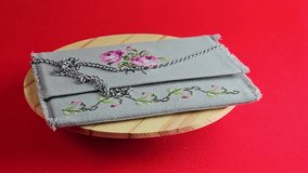 Handmade retro clutch bag on a red background. On the surface of the bag there is cross stitch. Ornament of roses. Vintage bag on a chain handle. Bag rotates on a wooden board.
 - Powered by Shutterstock - Get 15% off with code: PIKWIZARD15
