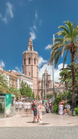 Panoramic timelapse hyperlapse of Plaza de la Reina in Valencia, Spain. Lively square with a historic church tower, bustling cafes and a central fountain with palms under the warm Mediterranean sky.