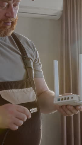 Vertical of bearded man as maintenance technician installing internet router and plugging in cable with lens flare effect