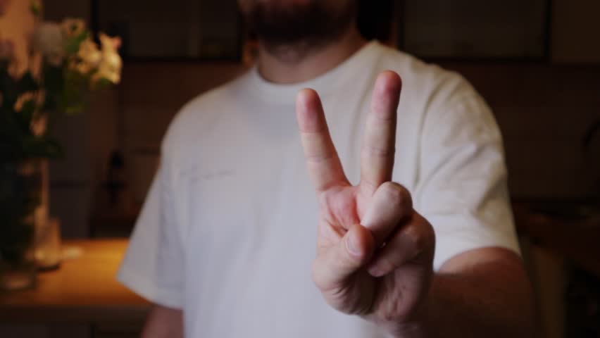 Man holding two fingers. Casual outfit, wearing shirt in a dimly lit room