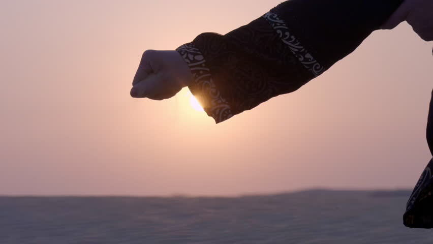 Arabic woman lady with Abaya cloth slow motion playing with sand during sunset in the desert sand dune