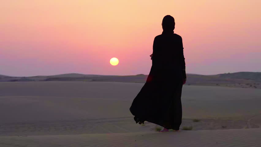 Arabic woman lady with Abaya cloth slow motion standing walking looking at the sun in the desert sand dune sunset
