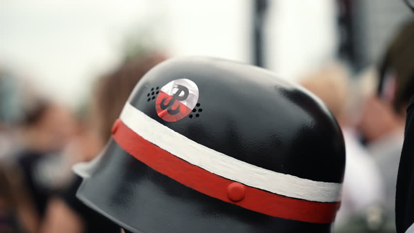 Close-up of a symbolic metal helmet with a Polish flag ribbon and the Warsaw Uprising emblem, captured during a commemorative event.