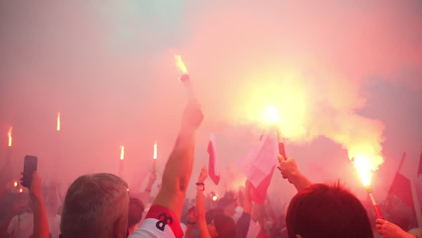 People commemorate Warsaw Uprising Day with red smoke flares during a peaceful march. Polish flags and the uprising symbol are visible through the smoke-filled square.