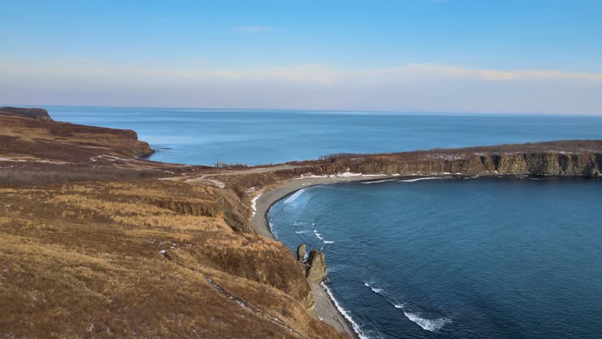 Side view of cape during winter. Waves crash against the rocky shoreline while the sea stretches to the horizon. Vyatlina Cape in Primorsky Krai, Russia.