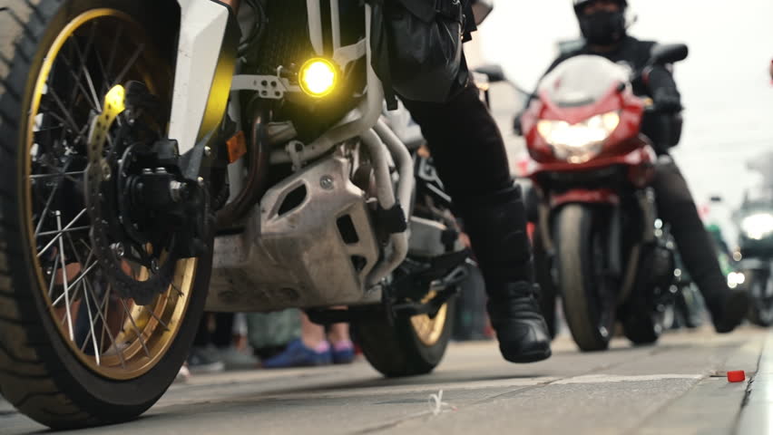 Motorcycle parade riding through a crowd, passing close to the camera at ground level.