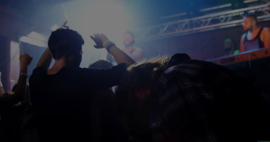 Beat intensifying driving two men dancing front row in music venue, stage lights pulsing with haze. Concert, nightlife, rave, dance, energetic, vibrant, atmosphere