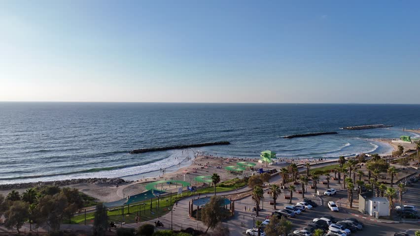 Aerial view of Ashkelon Beach featuring golden sands, clear blue waters, and the lifeguard hut standing prominently on the shore. A lively Mediterranean coastal scene captured in stunning 4K.

