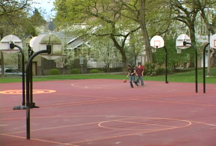 Group of men play basketball at park.