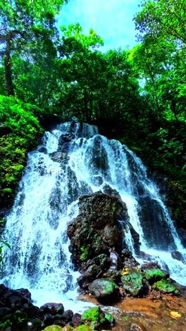 Real-time 4K footage of a tropical waterfall flowing through dense green forest vegetation. Natural ambient lighting, steady composition, and no people.