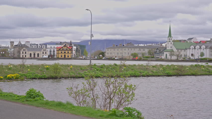 Woman walks along Tjornin lake in downtown Reykjavik on a cloudy day