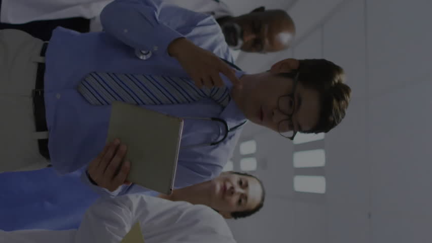 Animation of graphs, diverse doctor discussing patient reports while walking in hospital corridor. Trading boards, digital composite, report, business, stock market, teamwork, medical and healthcare. - Powered by Shutterstock - Get 15% off with code: PIKWIZARD15