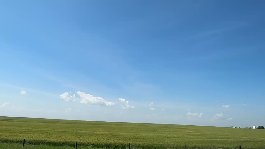 Driving past scenic farmland fields in the rural countryside, capturing open skies, agricultural landscapes, crops, grasslands, and peaceful farm views along a quiet country road in Alberta, Canada.