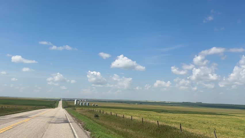Driving past scenic farmland fields in the rural countryside, capturing open skies, agricultural landscapes, crops, grasslands, and peaceful farm views along a quiet country road in Alberta, Canada.