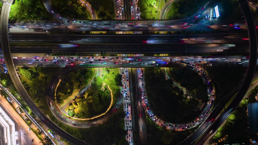 Aerial timelapse of Jakarta highway interchange at night. Bright traffic trails, glowing roads, and dynamic city infrastructure in Indonesia's capital.