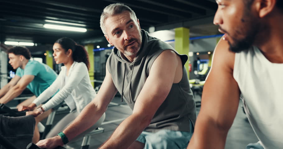 Men, cycling and fist pump with coach at gym for motivation, target or goals at fitness club. People, personal trainer and support with exercise bike, cardio workout or wellness at training center