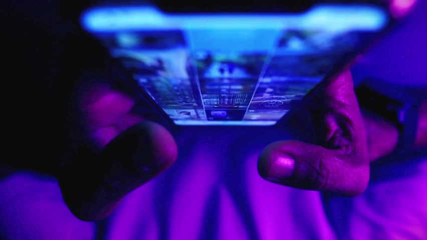 Close-up of hands holding a smartphone displaying a grid of images, illuminated by vibrant purple and blue neon lights.