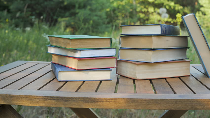 Stack of Hardcover Books on Wooden Table Outdoors, Educational literature arranged in nature setting during sunny summer day in forest meadow