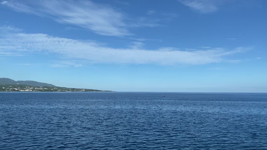 A tranquil, wide shot of the deep blue sea meeting a clear sky with a few wispy clouds. The video captures the gentle ripple of the water surface, creating a peaceful and soothing atmosphere.