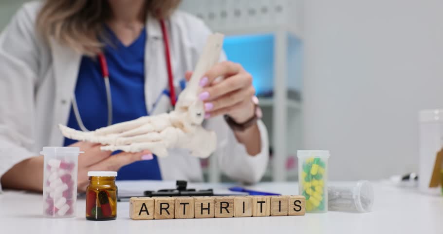Scrabble tiles form Arthritis placed in front of bone model evoking joint pain. Tablets and capsules nearby highlight medical fight with inflammation