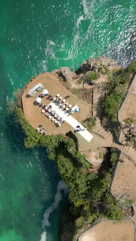 Aerial top view of wedding ceremony on scenic cliff overlooking turquoise waves in Bali, Indonesia. Tropical paradise with ocean, rocks, and romantic atmosphere.