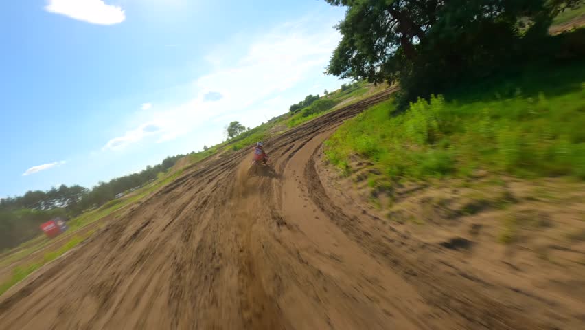 Cinematic slow motion FPV drone shot of motocross rider turning on dirt track. Dust flying, dynamic curves, and powerful movement in natural summer landscape.