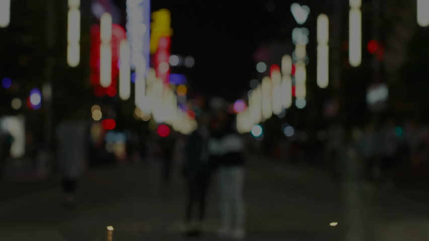 Japanese male adjusting headphones and mixing audio at desk with neon reflections dancing on glass. Neon, urban, nightlife, technology, concentration, reflection, ambient