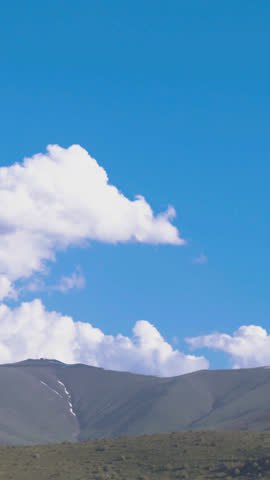 Panoramic summer field with lush green grass and a mountain backdrop. Time-lapse clouds drift gracefully over the peak, creating a serene and natural landscape perfect for travel and nature projects.