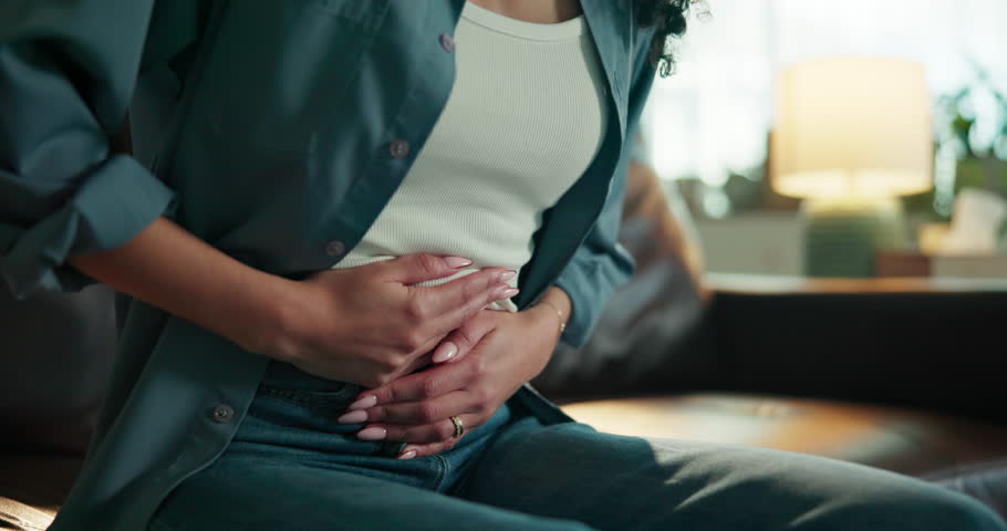 Stomach ache, hands and period pain with woman on sofa for endometriosis, menstruation and crisis. Abdomen, ovarian fibrosis and emergency with person in living room of home for inflammation