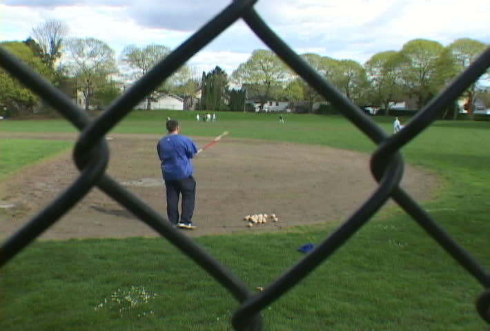Man coaches boys playing baseball in field.