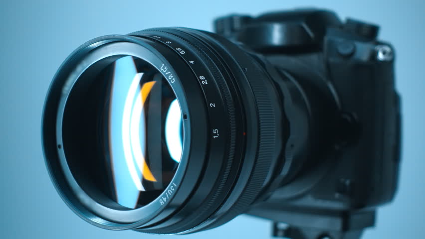 A professional camera on a tripod with an expensive lens with an aperture of 1.5 and a focal length of 85 mm, in which reflects the moving linear light. Closeup. Macro