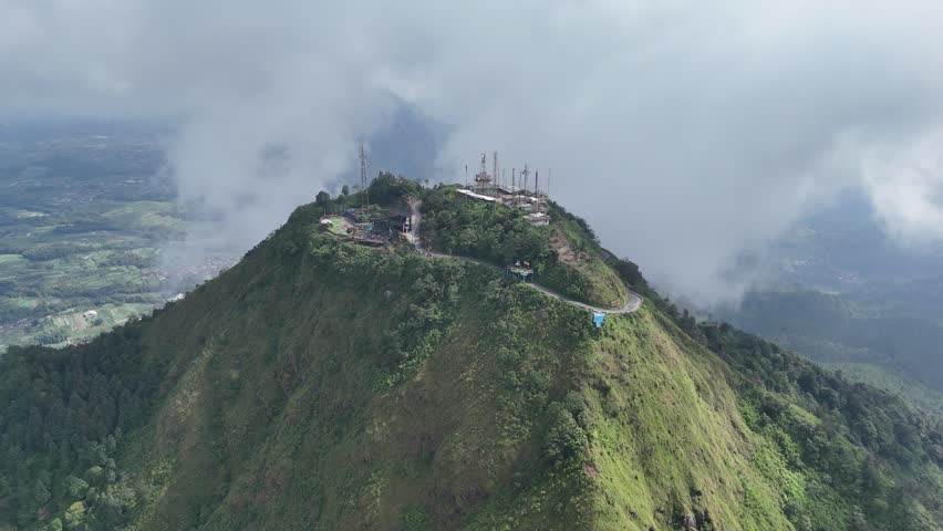 Drone footage of Telomoyo Mountain peak, Magelang. Floating clouds, a scenic tower, and a mountaintop café offer cinematic views and peaceful highland vibes